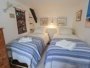 A bedroom with two single beds with blue striped blankets and folded towels on top at Cobblers Cottage in Langton Herring