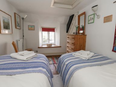 A bedroom with two single beds towels on beds wooden dresser and window at Cobblers Cottage in Langton Herring