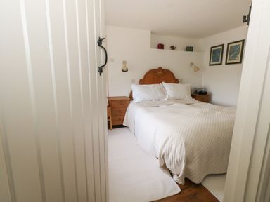A bedroom with a bed and wooden headboard two bedside tables and framed pictures on the wall at Cobblers Cottage in Langton Herring
