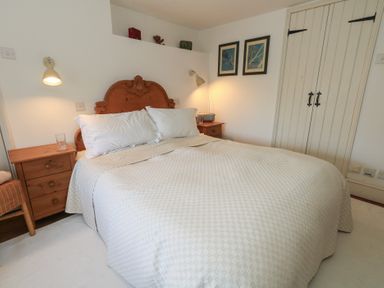 A bedroom with a double bed a wooden headboard bedside tables lamps framed pictures and a wardrobe at Cobblers Cottage in Langton Herring