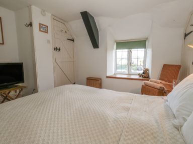 A bedroom with a bed a window wicker chair and a TV at Cobblers Cottage in Langton Herring