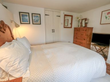 A bedroom with a bed white bedding wooden dresser TV and framed pictures on walls at Cobblers Cottage in Langton Herring