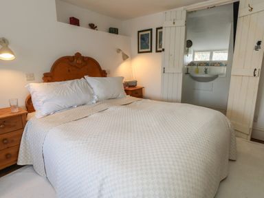 A bedroom with a double bed wooden headboard bedside tables with lamps and an open door to a bathroom at Cobblers Cottage in Langton Herring