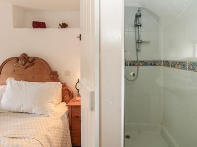 A bedroom with a wooden headboard and bedside table next to a bathroom shower with tiled walls at Cobblers Cottage in Langton Herring