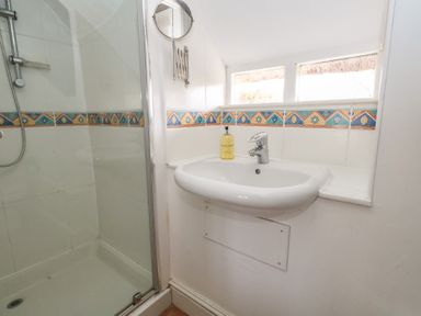 A bathroom with a shower enclosure and a wall-mounted sink with a soap dispenser at Cobblers Cottage in Langton Herring
