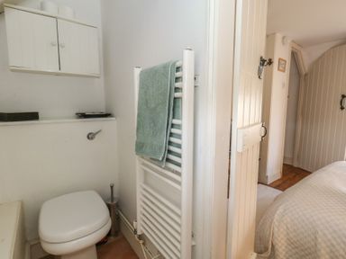 A bathroom with a toilet towel rack and door opening into a bedroom at Cobblers Cottage in Langton Herring