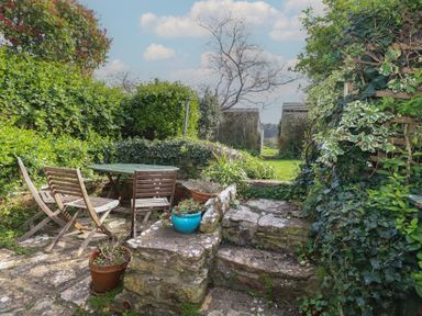 A garden patio with wooden chairs and table stone steps and green plants at Cobblers Cottage in Langton Herring