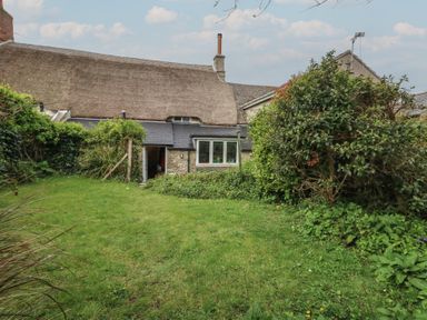 A backyard garden with grass and bushes behind a thatched cottage at Cobblers Cottage in Langton Herring