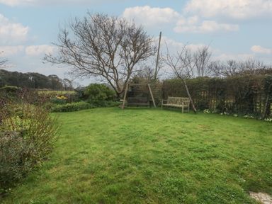 A garden with grass a wooden bench a garden swing and leafless trees at Cobblers Cottage in Langton Herring