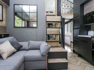 A living area with a grey sofa, staircase, kitchen cabinets, and a window at Woof Luxury Family Pod in Keswick
