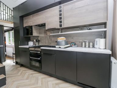 A kitchen with black cabinets a stove microwave kettle and containers at Woof Luxury Family Pod Keswick