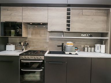 A modern kitchen with a gas stove oven microwave toaster sink kettle and storage containers at Woof Luxury Family Pod Keswick