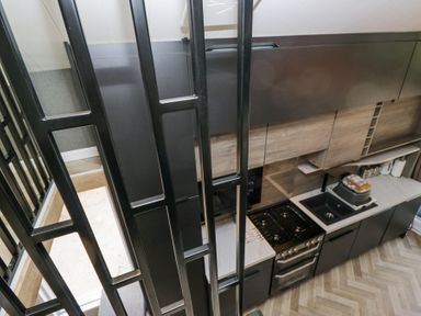 A kitchen with black cabinets a stove a sink and countertop behind a metal railing at Woof Luxury Family Pod in Keswick