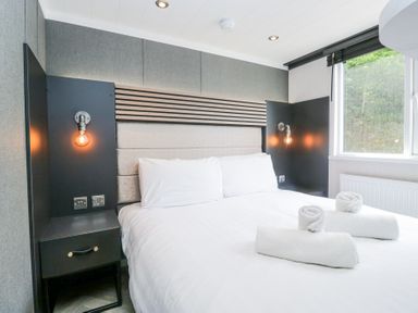 A bedroom with a double bed white linens wall lamps and a window at Woof Luxury Family Pod in Keswick