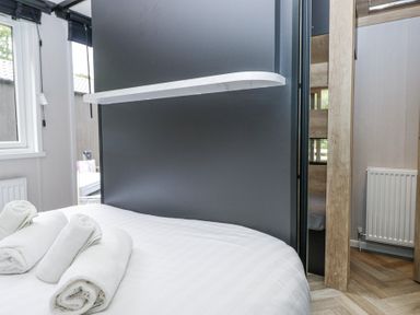 A bedroom with a bed with rolled white towels a window and a radiator at Woof Luxury Family Pod in Keswick