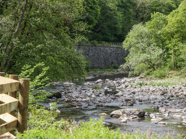 A river with rocks surrounded by trees and a wooden fence at Woof Luxury Family Pod in Keswick