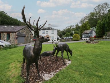 Bronze deer sculptures on grass with stone buildings and trees in the background at Lingy Luxury Family Pod in Keswick