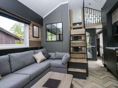 A living room with a gray sofa and a wooden coffee table next to stairs leading to a loft at Lingy Luxury Family Pod in Keswick