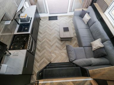 A small kitchen and living area with a grey sofa, coffee table, and stove viewed from above at Lingy Luxury Family Pod in Keswick