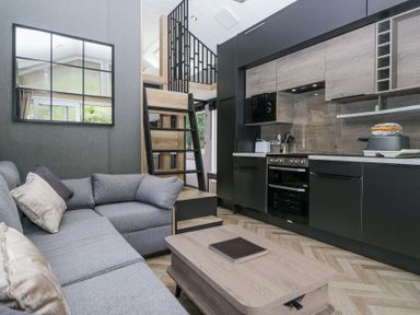 A living area with a grey sofa coffee table and a modern kitchen with black and wood cabinets at Lingy Luxury Family Pod in Keswick