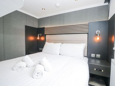 A bedroom with a double bed white pillows and rolled towels bedside tables with lamps at Lingy Luxury Family Pod Keswick