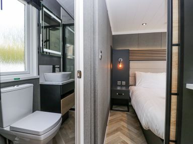 A bathroom with a toilet and sink next to a bedroom with a bed and nightstand at Lingy Luxury Family Pod in Keswick