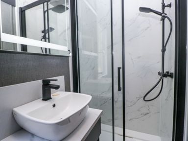 A bathroom with a white sink and black faucet next to a glass shower enclosure with a black showerhead at Lingy Luxury Family Pod Keswick