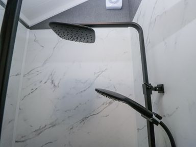 A shower area with a dual shower head system and marble-patterned wall panels at Lingy Luxury Family Pod in Keswick