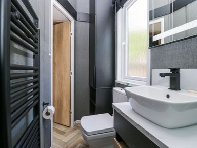 A bathroom with a toilet and sink next to a window and a door open to another room at Lingy Luxury Family Pod in Keswick