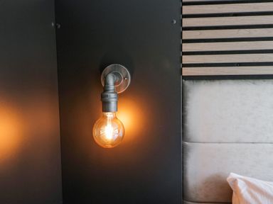 A wall-mounted light bulb next to a padded headboard with wooden slats at Lingy Luxury Family Pod in Keswick