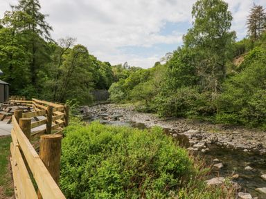 A wooden fence with picnic tables next to a rocky river surrounded by trees at Lingy Luxury Family Pod in Keswick