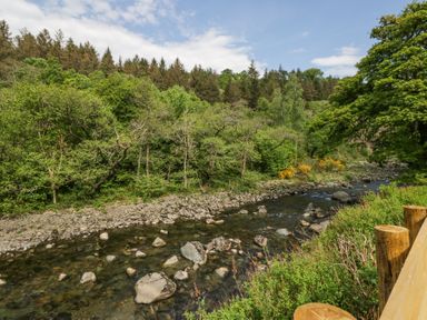 A river with rocks and green trees along the banks at Lingy Luxury Family Pod in Keswick