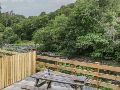 An outdoor seating area with a table and chairs near a river at Sail Luxury Family Pod in Keswick
