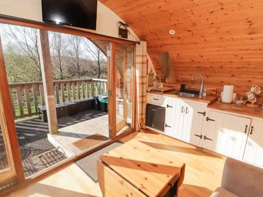 A small kitchen with wooden cabinets and countertop next to glass doors leading to a wooden deck at Cabanau Bach in Bedwas
