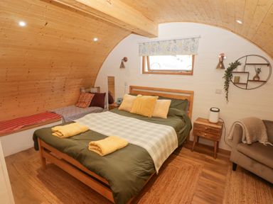 A bedroom with a double bed with pillows and folded towels a side table a chaise lounge and a wooden curved ceiling at Cabanau Bach in Bedwas