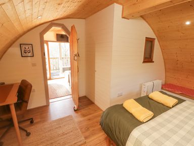 A curved wooden room with a bed with towels on it a desk and chair and an open door leading outside at Cabanau Bach in Bedwas