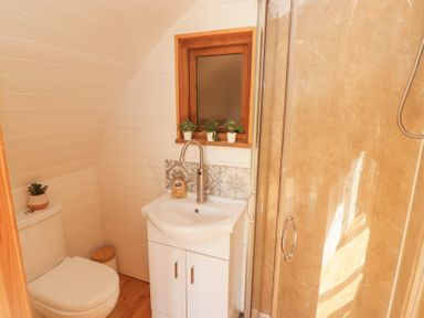 A bathroom with a toilet a sink cabinet a small window and a shower enclosure at Cabanau Bach in Bedwas