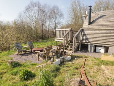 An outdoor area with wooden chairs and a fire pit near a wooden cabin with stairs at Cabanau Bach in Bedwas