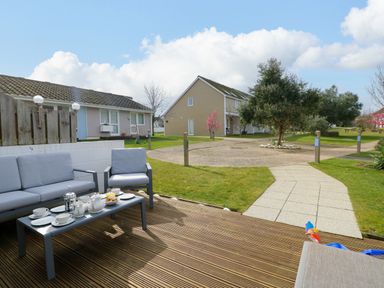 A patio with outdoor seating and a table set for tea outside houses with lawn and trees at Plimoth N9 in Yarmouth