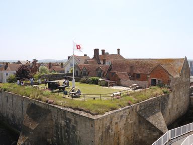 A historic fort with stone walls a grass-covered courtyard a flagpole and people walking and sitting at Plimoth N9 in Yarmouth