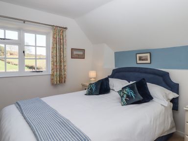 A bedroom with a bed pillows lamps and window with floral curtains at Badger's Den in Budleigh Salterton