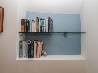 A built-in bookshelf with two shelves holding books and a small figurine at Badger's Den in Budleigh Salterton