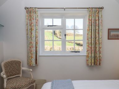 A bedroom window with floral curtains and a patterned chair next to the wall at Badger's Den in Budleigh Salterton