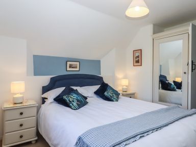 A bedroom with a double bed with blue headboard two bedside tables with lamps and a mirrored wardrobe at Badger's Den in Budleigh Salterton