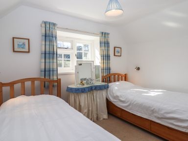 A bedroom with two single wooden beds a window with blue and beige checked curtains and a small round table with mirrors at Badger's Den in Budleigh Salterton