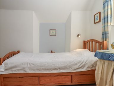 A bedroom with a single wooden bed with storage drawers and a small round table covered with cloth at Badger's Den in Budleigh Salterton