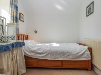 A bedroom with a single wooden bed with white bedding next to a dressing table with a mirror and curtains at Badgers Den in Budleigh Salterton