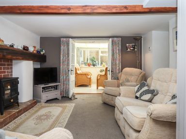 A living room with beige armchairs a television floral curtains and a small sitting area beyond at Badger's Den in Budleigh Salterton