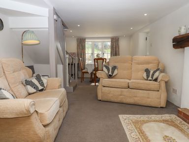 A living room with beige sofas and animal face cushions a dining table by a window and a lamp at Badger's Den in Budleigh Salterton