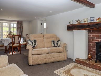 A living room with beige sofa two cushions fireplace and dining table with chairs and flowers at Badger's Den in Budleigh Salterton